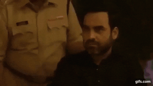 a man with a beard is sitting in front of a police officer and talking to him .